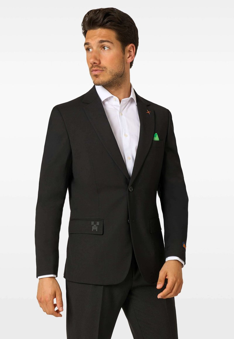 Čierna saková bunda s moderným strihom, ktorá má dve predné vrecká, zelený vreckový štvorcový a dekoratívne prvky na klopách a vreckách.