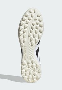 Černobílá sportovní bota s texturovanou bílou gumovou podrážkou s kuželovitými hroty, na boku označená nápisem "PREDATOR".