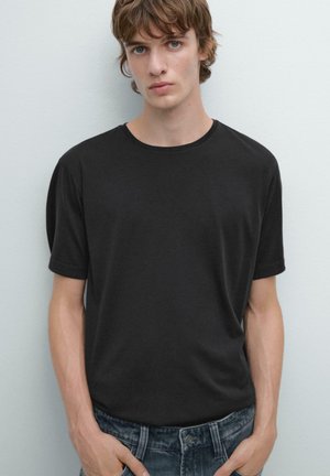 T-shirt noir à col rond en tissu lisse, avec des manches courtes et une coupe décontractée, associé à un jean en denim sombre.