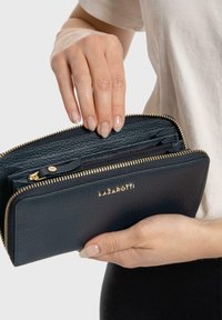 Navy leather wallet with a textured finish, gold zipper, and logo. It features multiple compartments and a zippered pocket, held in a hand.