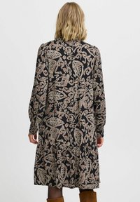 Rochie neagră cu mâneci lungi, cu un model floral în crem și bej, având o fustă în volane și manșete strânse.