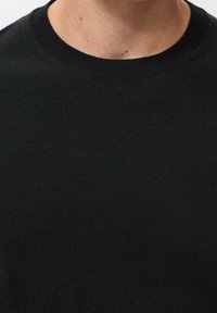 Pull en maille noire avec un col rond, présentant une texture lisse et une coupe ajustée. Aucun motif ou accent visible.