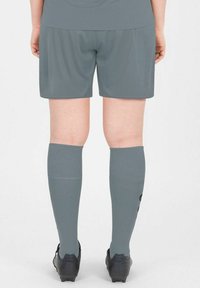 Shorts atletici grigi con una superficie liscia, abbinati a calzini grigi fino al ginocchio. Footwear con tacchetti neri e superficie textured.