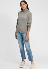 Grijze gebreide trui met een hoge kraag en geribbelde zoom, gecombineerd met lichtblauwe jeans en sneakers met roze accenten.