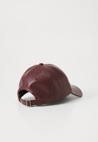 Burgunderfarget lærbaseballlue med sømdetaljer, buet skjerm og justerbar stropp bak. Glatt tekstur, seks-panel design.