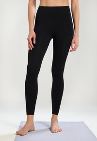 Leggings neri realizzati in tessuto elasticizzato con una vita alta, design aderente e costruzione senza cuciture, presentati su un tappetino chiaro.