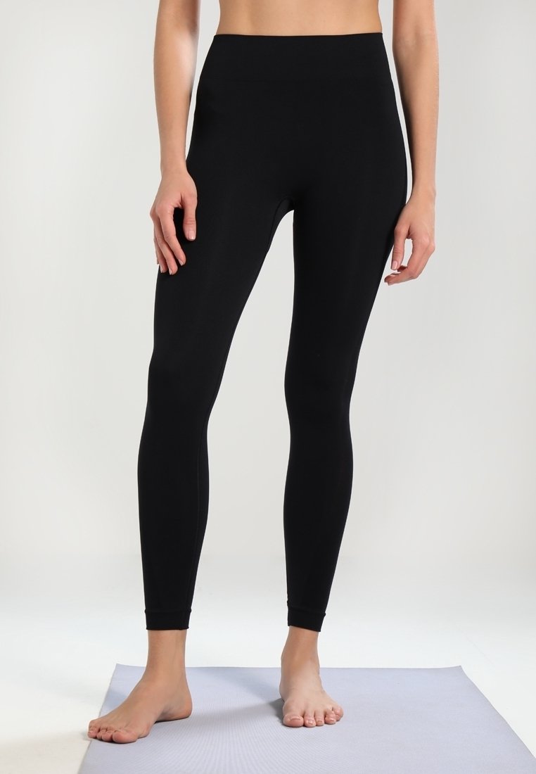 Leggings neri realizzati in tessuto elasticizzato con una vita alta, design aderente e costruzione senza cuciture, presentati su un tappetino chiaro.