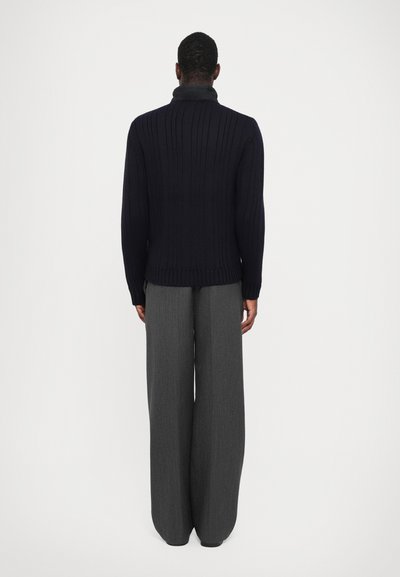 Un pull navy à côtes avec un col montant, associé à un pantalon large gris. Le tissu semble texturé et chaud, avec un design ajusté.