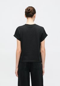 Zwart T-shirt met korte mouwen en een losse pasvorm, gemaakt van zacht materiaal, met opgerolde manchetten en een rechte zoom, gecombineerd met zwarte broek met wijde pijpen.