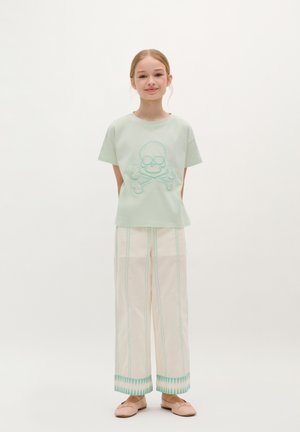 Mint green cotton t-shirt with skull and crossbones design, paired with cream wide-leg pants featuring turquoise stitching and patterned cuffs.