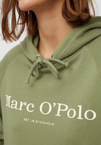 Olijfgroene hoodie met een trekkoord, met daarop het geprinte logo "Marc O’Polo" en "EST. IN STOCKHOLM." Zachte stof en een ontspannen pasvorm.