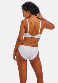 Sujetador blanco y bragas a juego mostrados desde atrás. El sujetador cuenta con tirantes ajustables y un cierre de gancho. Las bragas tienen un diseño texturizado y con patrón.