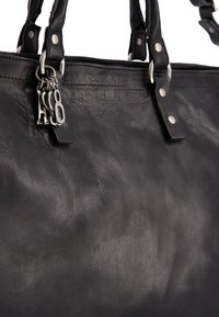 Sort læderhandtaske med en tekstureret overflade, sølv hardware og en logo-charms. Har to robuste håndtag og synlige syninger.
