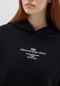 Zwarte hoodie met witte geborduurde tekst met een Parijse adres en datum. Zacht, gestructureerd stof en een casual ontwerp.