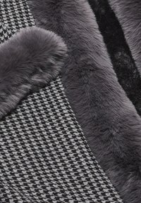 Kankaan pinta, jossa on mustavalkoinen houndstooth-kuvio, jota täydentää pehmeä ja ylellinen harmaa keinoturkisreuna.