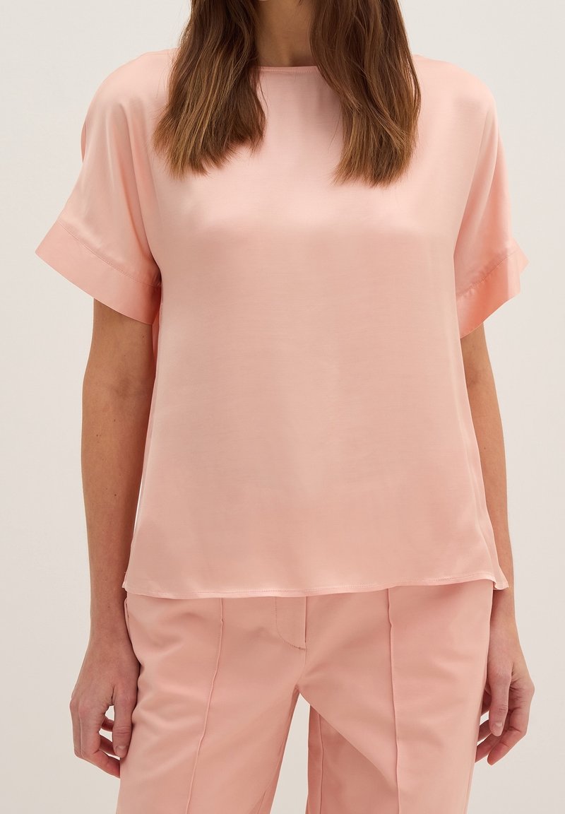 Haut en soie rose à manches courtes et col rond, présentant une texture lisse et brillante ainsi qu'une coupe décontractée. Associé à un pantalon assorti.