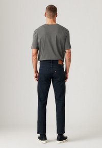 Gray cotton t-shirt and dark blue jeans with a leather patch. The jeans have a straight cut and a smooth texture. Black shoes complete the look.