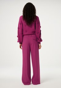 Fuchsia trui met textuur en bloemdetails, gecombineerd met fuchsia broek met wijde pijpen. Zacht materiaal, losse pasvorm en uniforme kleur.