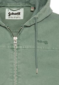 Grøn hættejakke med frontlynlås, broderet Schott NYC-logo på brystet, indvendig mærkat og amerikansk flag-størrelseetiket L.