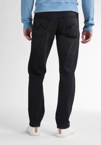 Zwarte denim jeans met een slim fit, voorzien van achterzakken met gebogen stiksels, gedragen met een lichtblauwe sweatshirt en witte sneakers.
