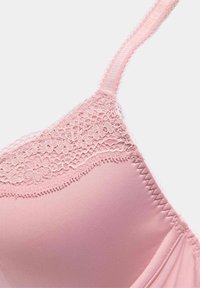 Reggiseno rosa chiaro con una texture liscia simile alla seta, con bordino in pizzo lungo il bordo superiore e cuciture decorative sulla coppa.