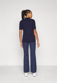 Navy knitted short-sleeve shirt with ribbed texture, paired with dark blue flared pants and white sneakers, viewed from the back.