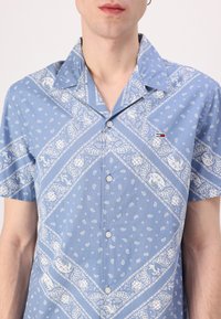 Camicia a maniche corte di colore azzurro chiaro con motivo paisley bianco e dettagli. Presenta un colletto a punta e chiusura con bottoni. Dettaglio con logo Tommy Hilfiger.