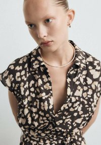 Bruine korte mouwen blouse met een luipaardprintpatroon in crèmekleur en beige. Voorzien van een kraag en een knoopjessluiting aan de voorkant, zachte stoftextuur.