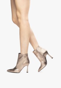 Bottes chelsea en bronze métallique avec un bout pointu, un talon aiguille haut et une fermeture éclair ; texture lisse avec un éclat subtil.