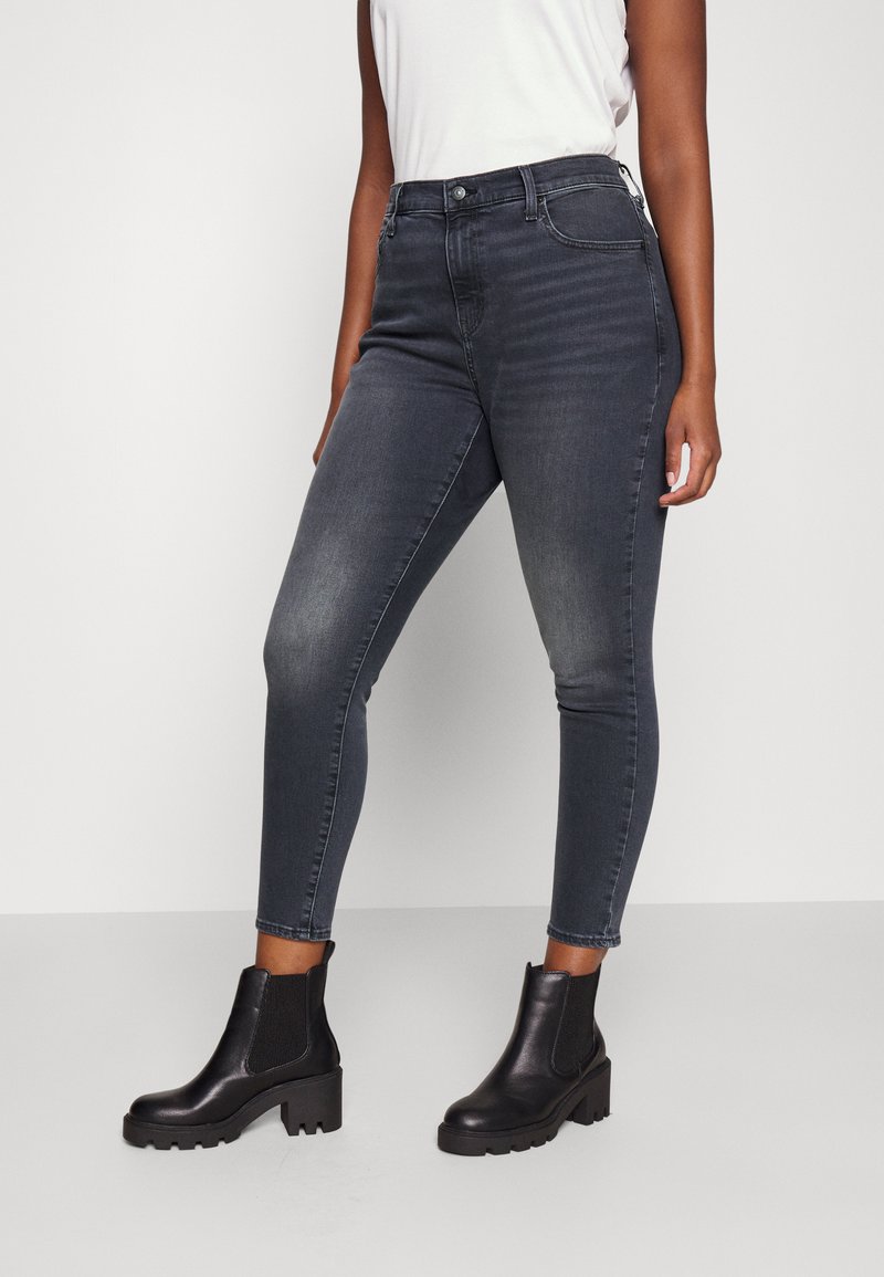 Dunkelgraue Skinny-Jeans mit mittelhohem Bund, faded Waschung und eng anliegendem Schnitt, kombiniert mit schwarzen Stiefeletten mit einer klobigen Sohle.
