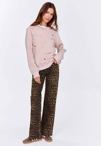 Světle růžová mikina s vyšívanými srdci a textem, v kombinaci s volnými kalhotami s leopardím potiskem a hnědými nazouvacími botami.