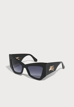 Lunettes de soleil noires surdimensionnées avec un design anguleux, verres dégradés et accent logo ailé doré sur la branche. Fabriquées en plastique.