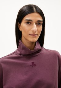 Lila Sweatshirt mit hohem Kragen, versehen mit einem dezenten gestickten Design auf der Brust. Weicher Stoff mit glatter Textur.
