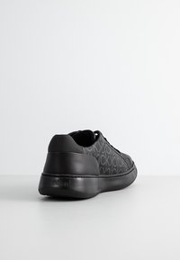 Baskets noires avec une tige texturée présentant un motif logo, talon en cuir noir lisse et semelle en caoutchouc contrastante.