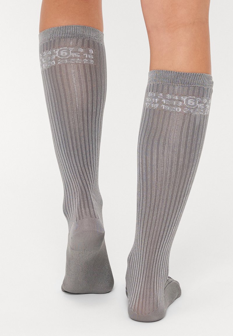 Chaussettes grises montantes avec texture côtelée et détail du logo blanc sur le revers. Tissu lisse, forme ajustée et conception de orteil sans couture.