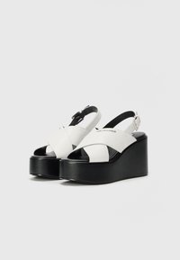 Hvite plattform sandaler med kryssbånd, svart kile såle og ankelstropp, med glatt materiale og elegant design.