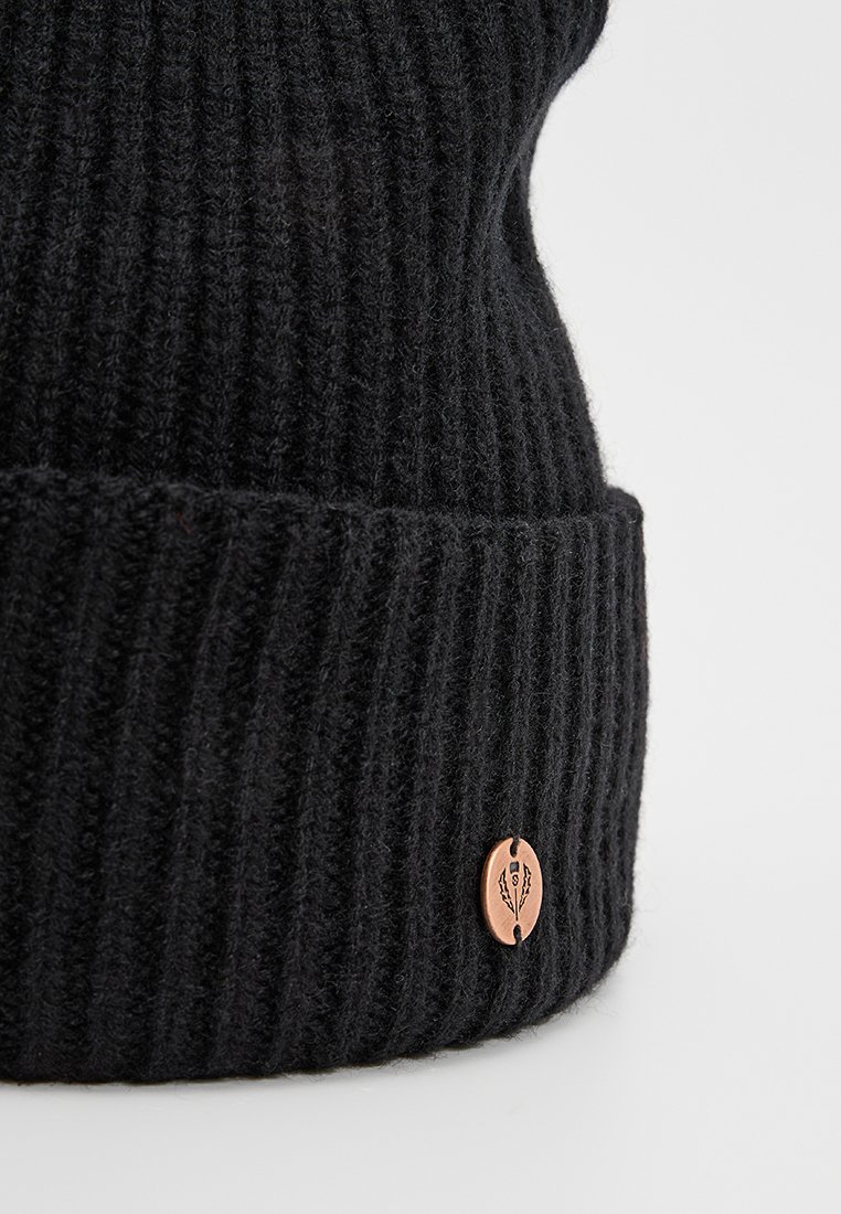 Czarna dziany czapka beanie o prążkowanej fakturze z miedzianym logo na mankiecie. Materiał wydaje się miękki i ciepły.