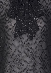 Tessuto di abito nero con ricami testurizzati e paillettes sparse. Include un grande fiocco decorativo all'scollatura.