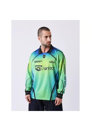 Mann mit kurzen Haaren trägt ein langärmliges Sporttrikot in grün-blauem Farbverlauf mit schwarzem Text und Designs und schaut zur Seite.