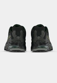 Pantofi sport negri cu accente verzi, având un călcâi texturat din fibră de carbon, talpă groasă din cauciuc și o parte superioară din plasă respirabilă.