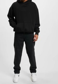 Czarna bluza z kapturem z kieszenią z przodu, zestawiona z czarnymi dżinsami i białymi sneakersami z czarnym logo. Casulowy design, miękki materiał.