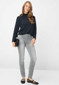 Top a maniche lunghe color blu navy, jeans slim fit grigio chiaro, ballerine nere intrecciate, in mano una pochette nera. Design semplice; tessuto dalla texture liscia.