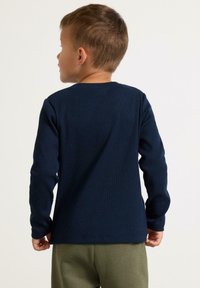 Mörkblå långärmad skjorta i ribbat tyg, med rundad halsringning och figurnära ärmar. Slät textur, enkel design.