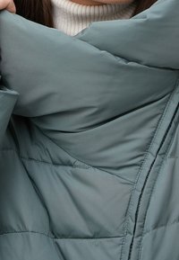 Padded jacket v tlumené modro-zelené barvě, s vysokým límcem, hladkým povrchem, zipovým zapínáním a prošívaným designem s viditelnými švy.
