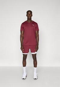 Bordeaux sportieve t-shirt en short set, gemaakt van ademend materiaal, met een slimfit ontwerp en witte accenten. Witte sportschoenen dragen.
