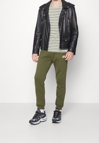 Svart läderbikerjacka, grönrandig T-shirt, olivgröna mjukisbyxor och svarta sneakers med grå accenter.