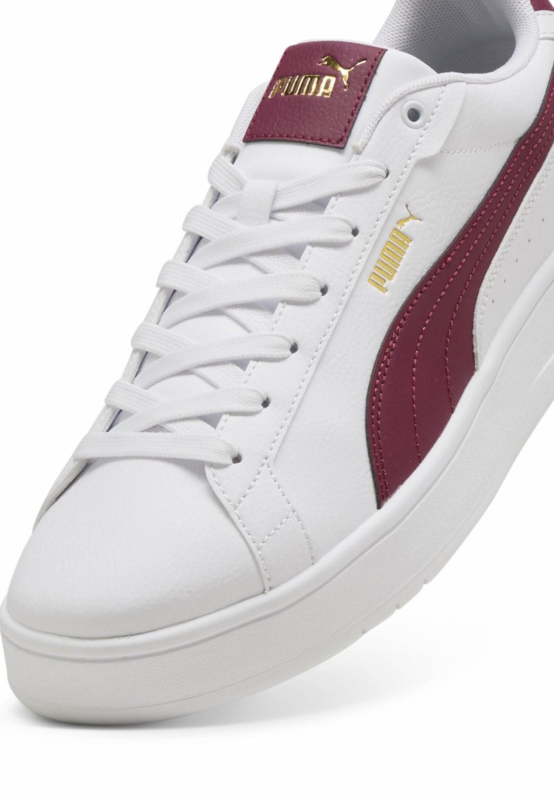 Białe skórzane sneakersy z bordowymi akcentami i fakturowanym bordowym paskiem na pięcie. Posiadają sznurowane zapięcie i gumową podeszwę. Złoty detal logo.