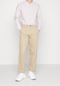 Ljusgrå långärmad skjorta med rundad krage och knappar, kombinerad med beige chinos och vita sneakers. Enkel och figursydd design.