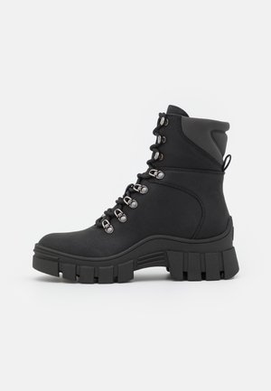 Botte de combat noire à lacets avec semelle épaisse à crampons, œillets métalliques, col rembourré et languette à l'arrière.