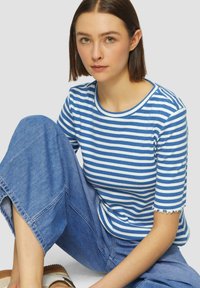Camiseta de rayas azules y blancas con escote redondo y dobladillos de mangas con forma de concha, combinada con pantalones de mezclilla ligeros y holgados de color azul.